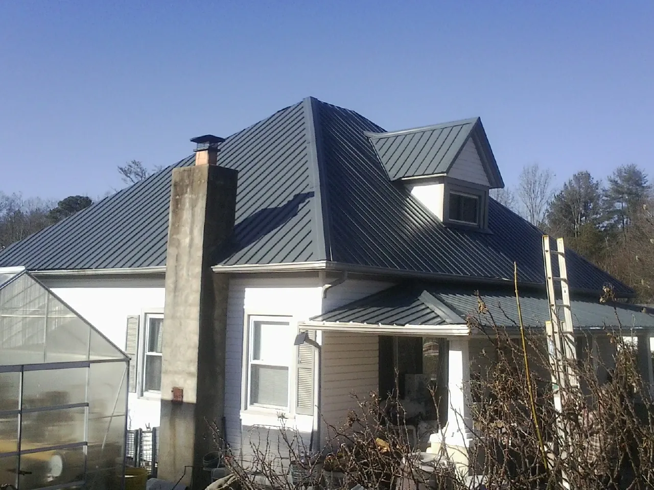 Dark blue standing seam metal roof on a white farmhouse with dormer in Moosic