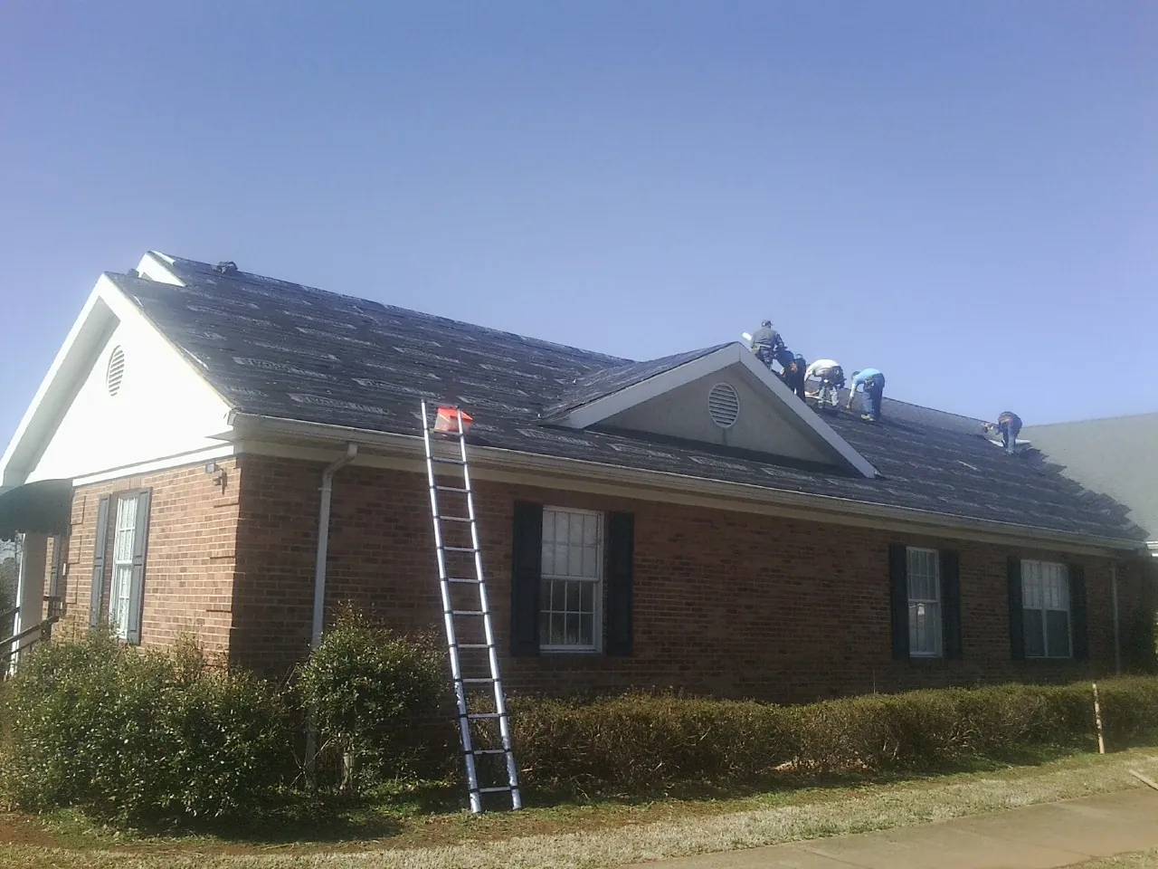 Crew tearing shingles off a brick ranch roof with a ladder set — Emergency Roof Repair work by our crew in Moosic