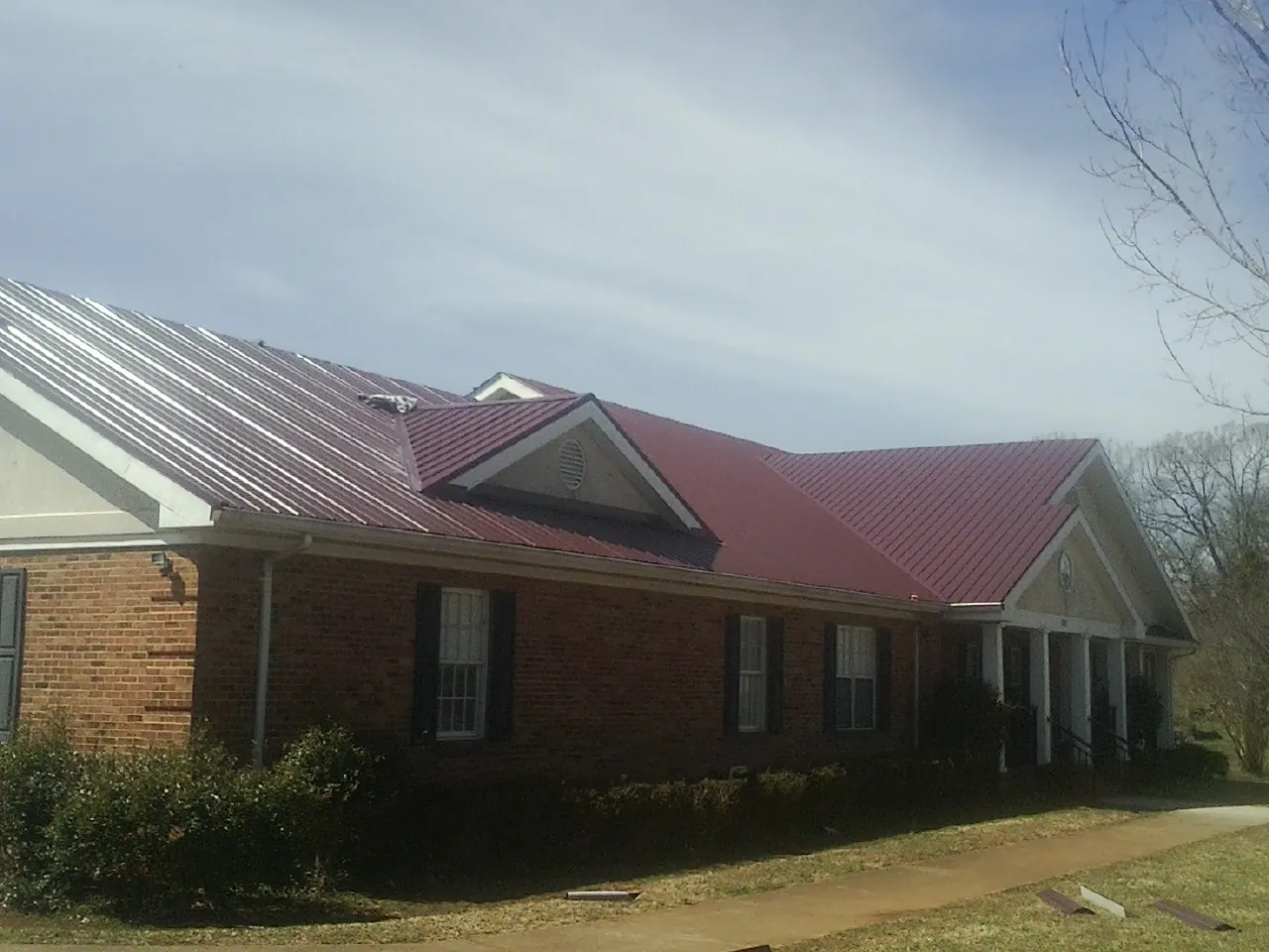 Red metal roof with gabled entries on a long brick building, from a Hail Damage Roof Repair job in Moosic