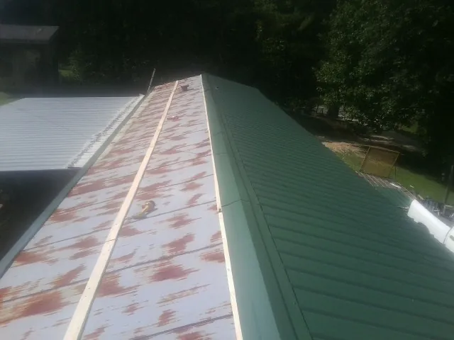 Old rusted panels beside newly installed green metal roofing — Wind Damage Roof Repair by Roofing Brothers in Moosic