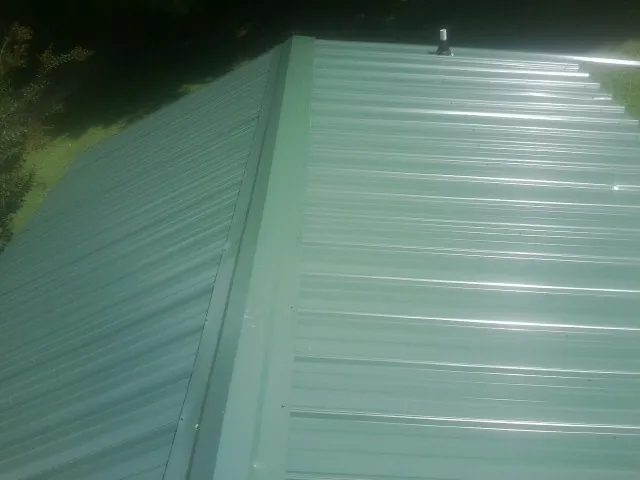 New green metal panels meeting at the ridge of a roof — Flat Roof Repair work by our crew in Moosic