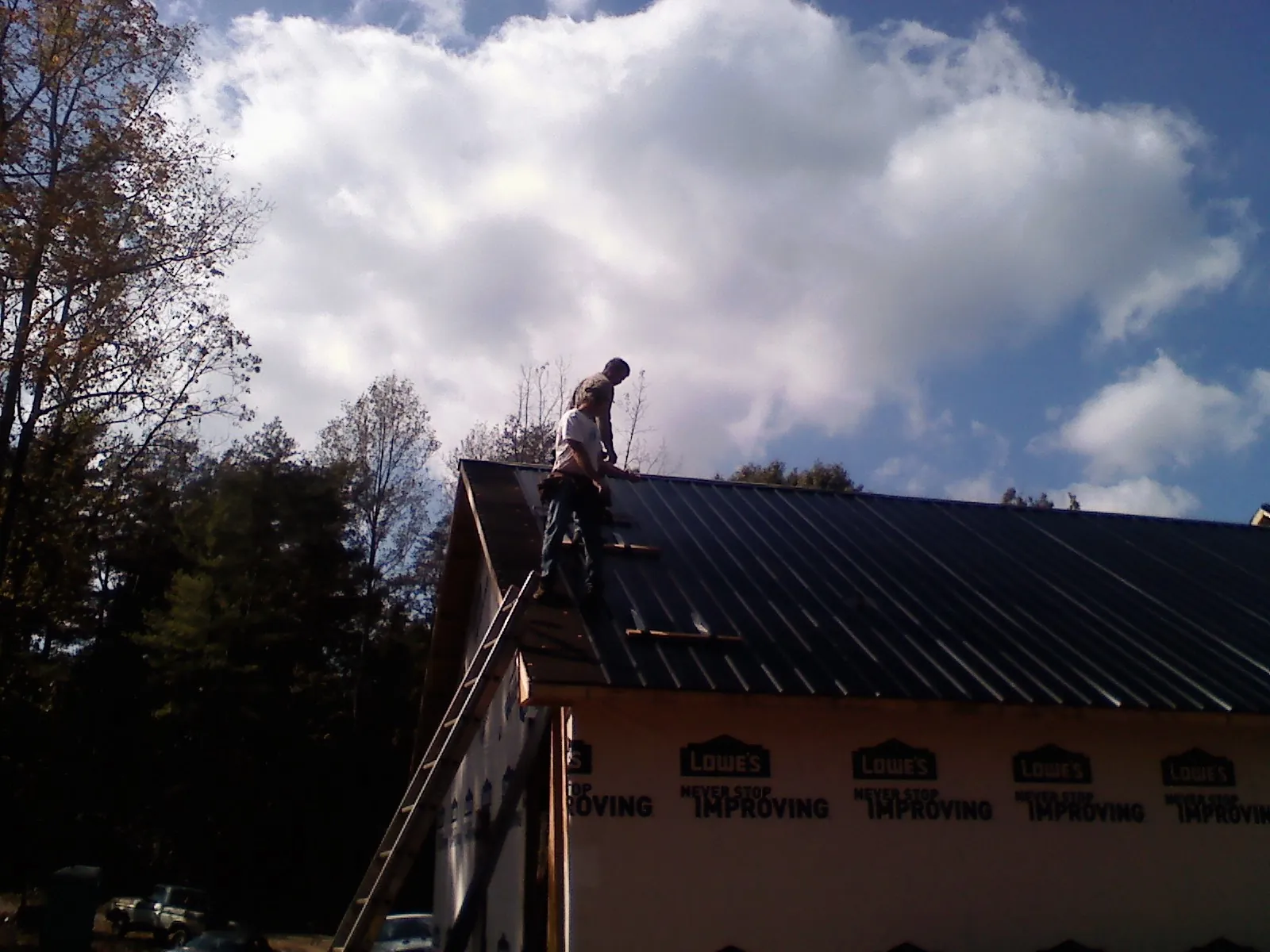 Roofer fastening dark metal panels high against a cloudy sky, from a Roof Inspection job in Moosic